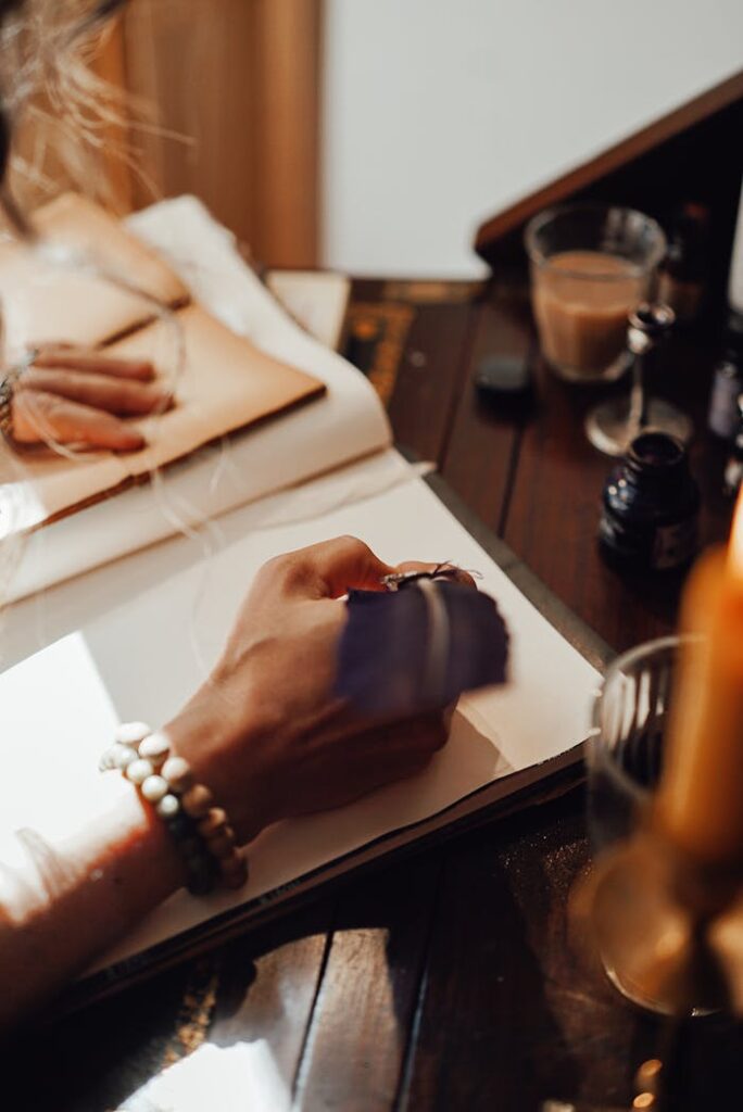 Crop anonymous female writer taking notes in copybook with feather at vintage table in sun ray at home